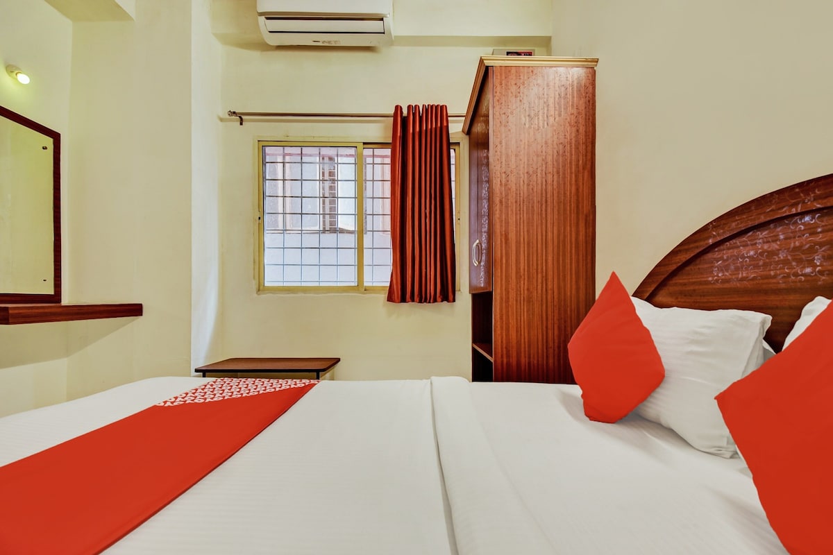 A hotel room with a bed, a wooden wardrobe, a window with curtains, and a mirror on the wall.