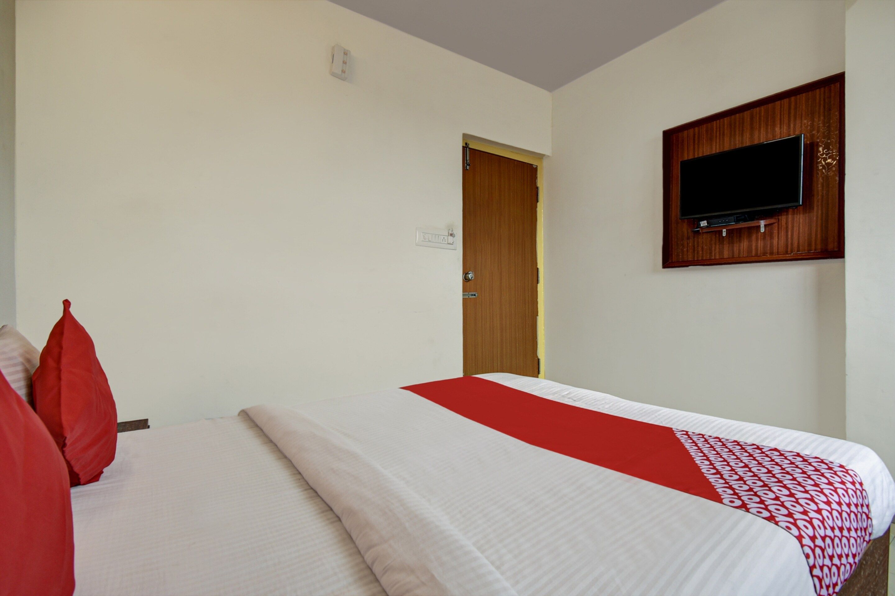 A hotel room with a bed, a television mounted on the wall, and a door leading to another room.