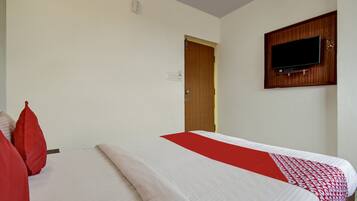 A hotel room with a bed, a television mounted on the wall, and a door leading to another room.