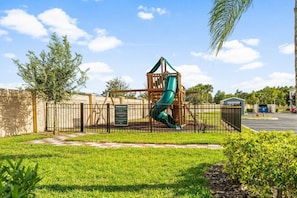 A playground with a slide and climbing structure, surrounded by a fence and greenery. - 12 min to Disney 3BR Home w/ Resort Access (Kissimmee)