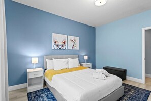 A bedroom with a bed, two bedside tables, a nightstand, a bedside lamp, a rug, and two wall art pieces. - 12 min to Disney 3BR Home w/ Resort Access (Kissimmee)