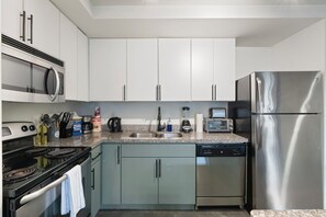 A modern kitchen with white cabinets, a stainless steel refrigerator, a built-in microwave, a stove, and a dishwasher. - Chic 2BR | Pool | W/D | Wi-Fi Near Arts District (Phoenix)