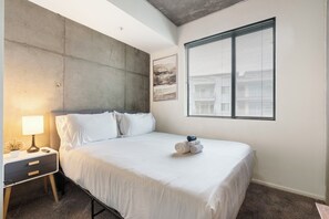 A bedroom with a bed, bedside table, lamp, and a window with blinds. - Chic 2BR | Pool | W/D | Wi-Fi Near Arts District (Phoenix)