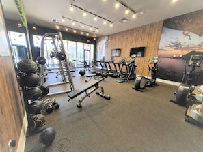 A gym with cardio machines, weightlifting equipment, and a large mirror. - 7562 Magic Village 8 Guests 4 Suites 8 min Disney (Kissimmee)
