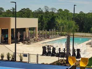 Un espace piscine avec des chaises longues et des parasols, un bâtiment doté de grandes fenêtres et une piscine entourée d’une clôture.