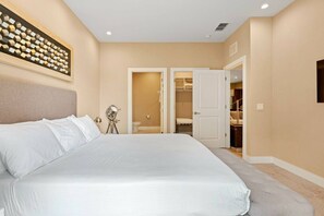 A bedroom with a large bed, a bedside table, a wall-mounted light, and a door leading to a bathroom. - 7562 Magic Village 8 Guests 4 Suites 8 min Disney (Kissimmee)