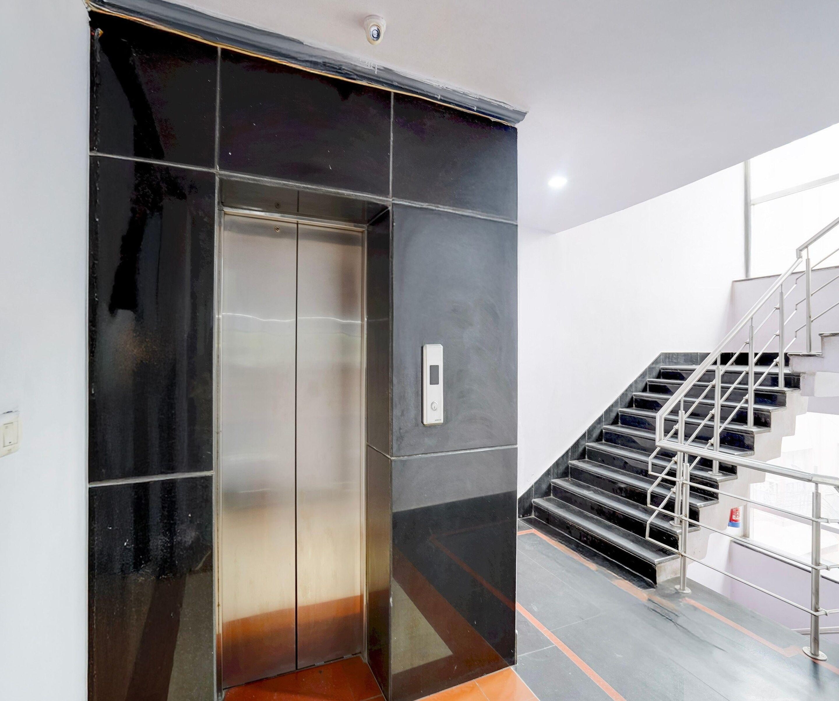 A modern elevator with a metallic finish, adjacent to a staircase with metal railings.