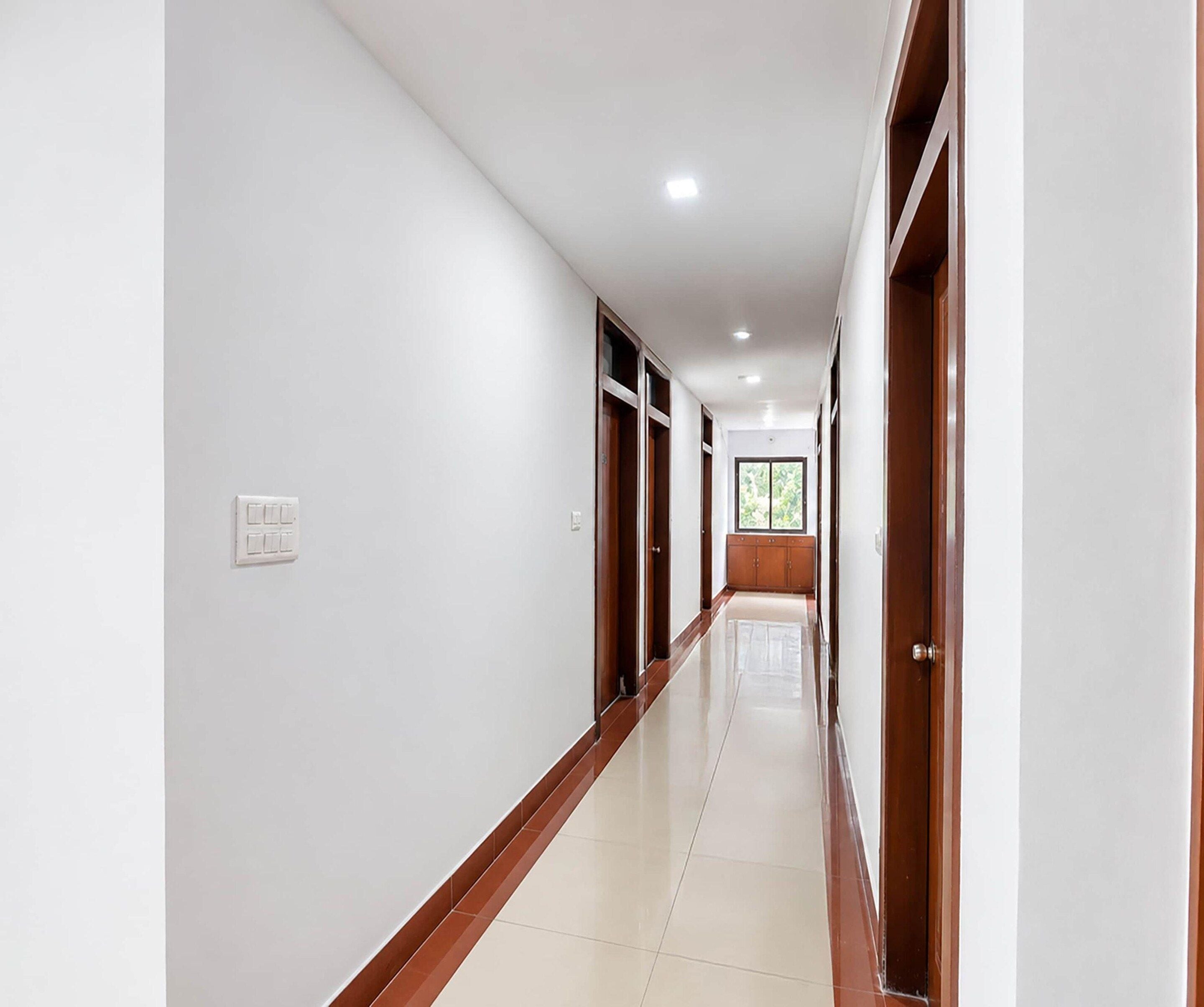 A corridor with white walls, wooden doors, and a tiled floor.