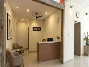 A reception area with a reception desk, chairs, a ceiling fan, and a clock on the wall. - Classic Hotel Sika Inn (Puducherry)