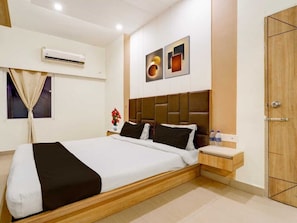 A hotel room with a bed, bedside table, wall-mounted air conditioning unit, and a door. - Classic Hotel Sika Inn (Puducherry)
