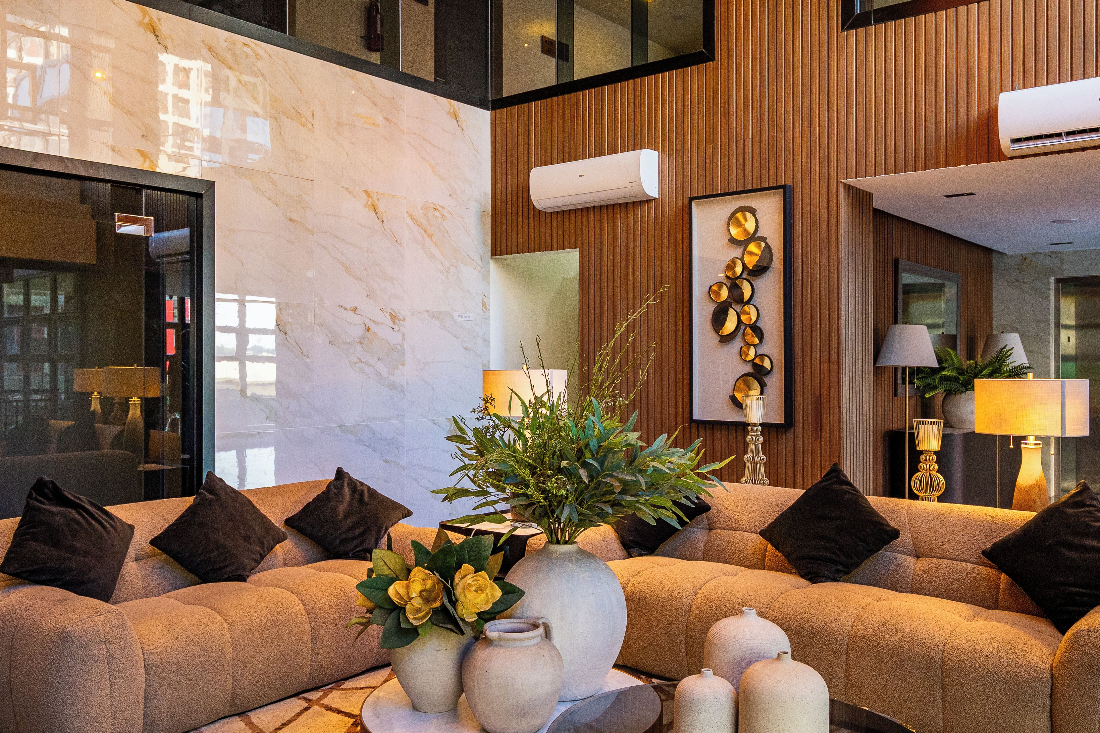 A modern lobby with a marble floor, a sofa set, a vase with flowers, and a decorative wall piece.