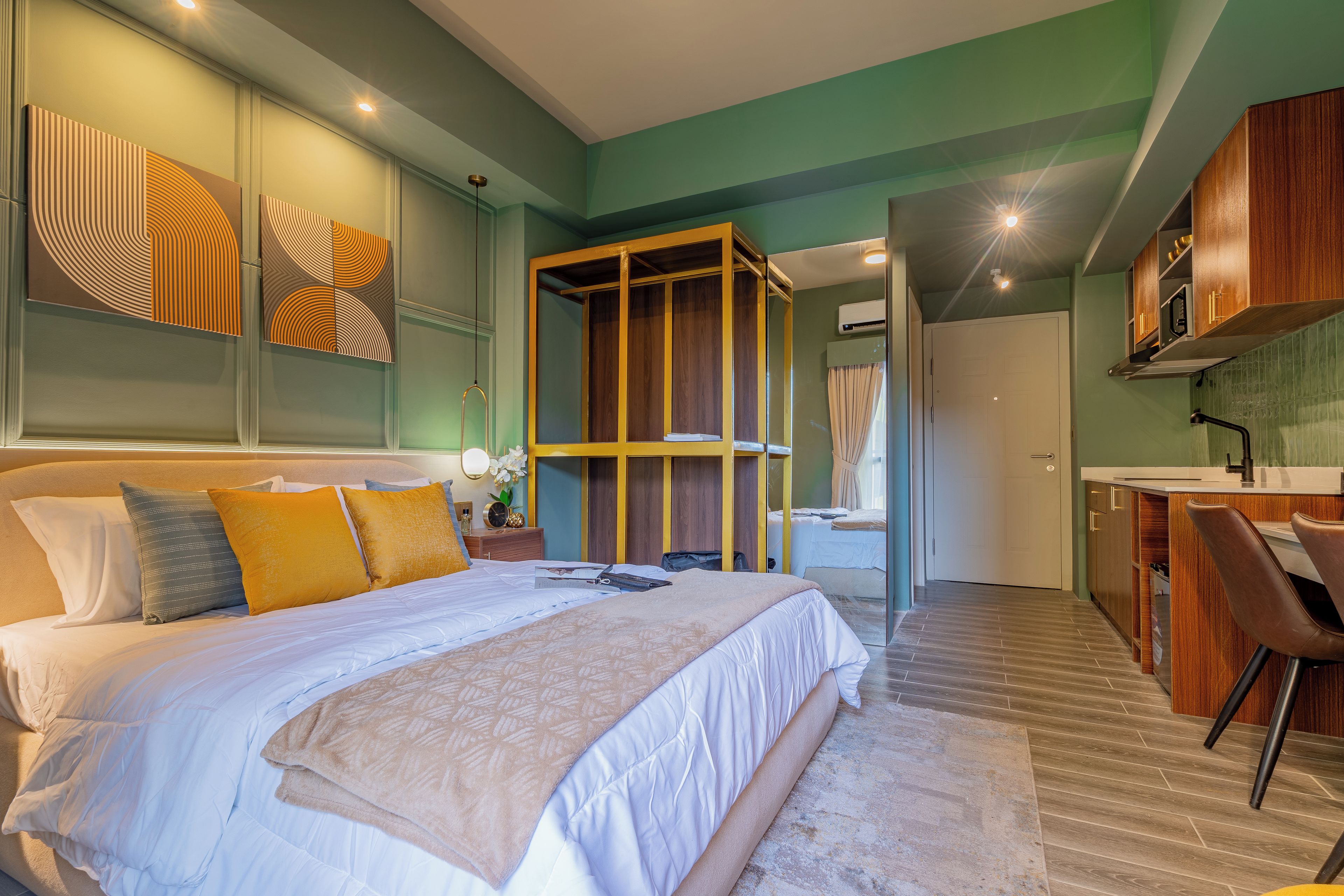 Una habitación de hotel moderna con una cama grande, un armario de madera, un baño con ducha y una kitchenette.