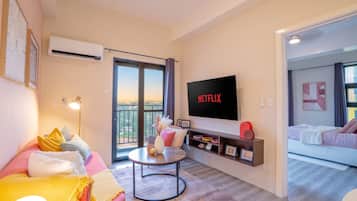 A modern living room with a flat-screen TV, a sofa, a coffee table, and a balcony with a view.