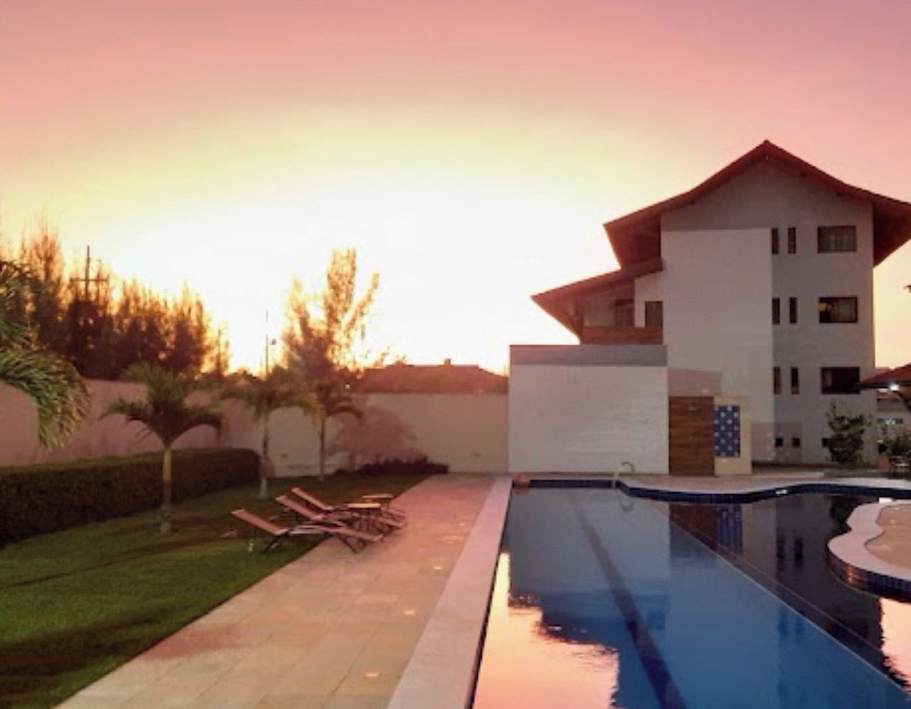 A modern building with a swimming pool, lounge chairs, and a well-maintained lawn.