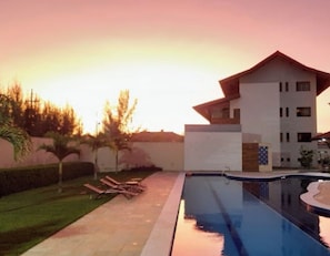 A modern building with a swimming pool, lounge chairs, and a well-maintained lawn.