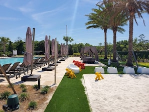 A poolside area with lounge chairs, umbrellas, and artificial palm trees. - 6 min to Disney - Modern 4suite Home (Kissimmee)