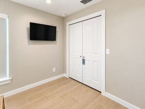 Habitación con televisor de pantalla plana montado en la pared, una puerta blanca y piso de madera claro.