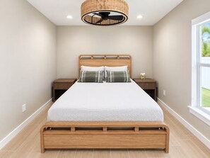 Un dormitorio con una cama de madera, dos mesitas de noche, un ventilador de techo y una ventana con vistas.