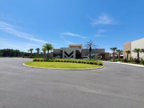 A modern building with a large parking lot, surrounded by palm trees and greenery. - Magic Village 8guests Jacuzzi 8 min Disney (Kissimmee)
