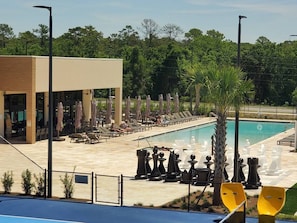 A pool area with lounge chairs and umbrellas, a building with large windows, and a fenced pool. - Magic Village 8guests Jacuzzi 8 min Disney (Kissimmee)