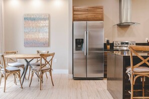 A modern kitchen with a stainless steel refrigerator, a built-in oven, and a wooden dining table with chairs. - Magic Village 8guests Jacuzzi 8 min Disney (Kissimmee)