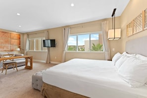 Une chambre avec un grand lit, une télévision, un bureau et une fenêtre avec des rideaux.