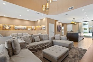 A modern living room with a sectional sofa, ottoman, and artwork on the walls. - Magic Village 3 Suites Jacuzzi 6min Disney (Kissimmee)