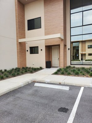 A modern building with a flat facade, large windows, and a parking area with marked spaces. - Magic Village 3 Suites Jacuzzi 6min Disney (Kissimmee)