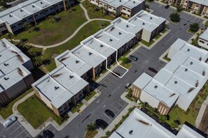 An aerial view of a residential area with multiple apartment buildings, a central parking lot, and surrounding greenery. - 7458 Magic Village 8 Guests - 8 min Disney (Kissimmee)