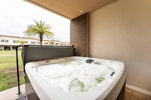 A hot tub with a wooden bench, a metal railing, and a view of a building and palm trees in the background. - 7458 Magic Village 8 Guests - 8 min Disney (Kissimmee)