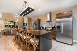 A modern kitchen with a large island, stainless steel appliances, and a dining area with wooden chairs. - 7458 Magic Village 8 Guests - 8 min Disney (Kissimmee)