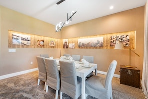 A dining area with a white table set for six, grey upholstered chairs, and a cityscape wall art display. - 7458 Magic Village 8 Guests - 8 min Disney (Kissimmee)