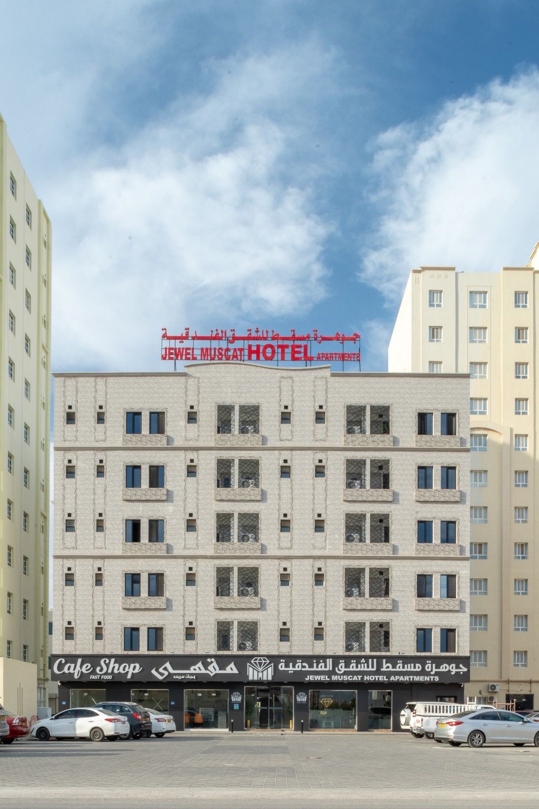 Un edificio de hotel con varios pisos, una cafetería en la planta baja y un cielo despejado al fondo.