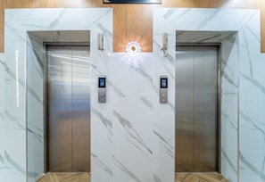 Two elevators with marble walls and wooden flooring, each with a digital display and a phone.