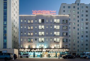 A hotel building with multiple floors, a cafe shop on the ground level, and a sign indicating it is the Jewel Muscat Hotel Apartments. - Jewel Muscat  (Seeb)