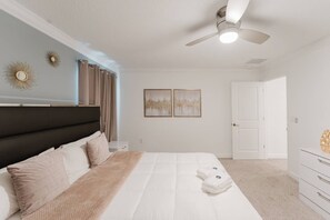 A bedroom with a bed, a ceiling fan, two wall-mounted artworks, a door, and a dresser. - Storey Lake 4BR Villa With Pool and Disney Rooms (Kissimmee)