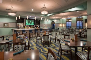 A hotel lobby with a bar area, multiple seating arrangements, and a large screen displaying a program. - Luxury 2BR Mickey Room Resort Amenities (Davenport)