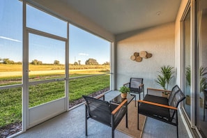 A balcony with a view of a grassy field, a table with chairs, and a wall-mounted decorative item. - Luxury 2BR Mickey Room Resort Amenities (Davenport)