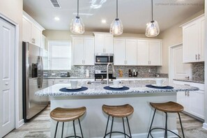 A modern kitchen with white cabinets, a granite countertop, stainless steel appliances, and three bar stools. - Modern Luxury 5BR Private Pool Near Disney (Kissimmee)