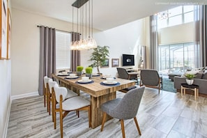 A modern living room with a dining area, a TV, and a large window. - Modern Luxury 5BR Private Pool Near Disney (Kissimmee)