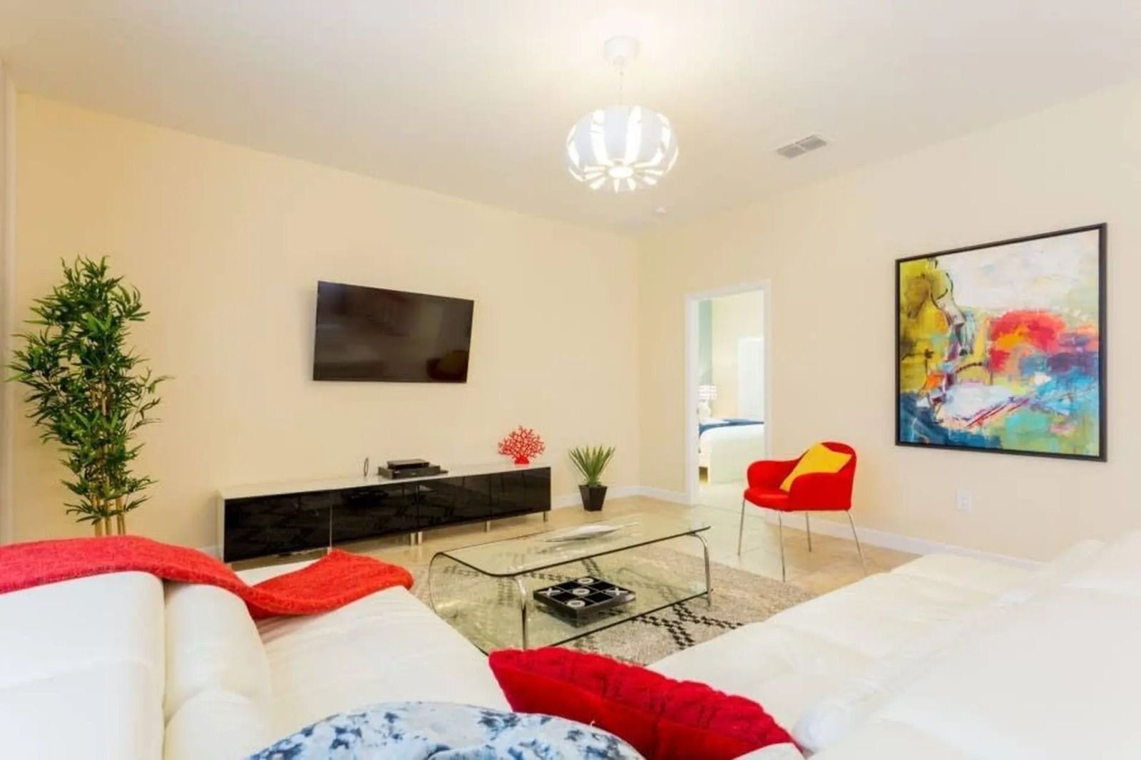 A modern living room with a flat-screen TV, a glass coffee table, a red chair, and a large abstract painting.