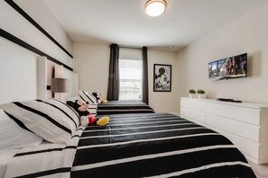 A bedroom with a bed featuring black and white striped bedding, a Mickey Mouse plush toy, and a framed picture of Mickey on the wall. - Elegant 4BR Home w/ Pool 10 Min to Disney! (Kissimmee)
