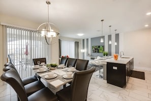 A modern dining area with a round table, black chairs, and a central light fixture. - Elegant 4BR Home w/ Pool 10 Min to Disney! (Kissimmee)