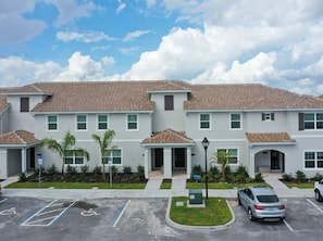 A multi-story building with a tiled roof, multiple windows, and a parking lot with marked handicapped spaces. - 4BR Townhome Private Pool 10 min to Disney (Kissimmee)