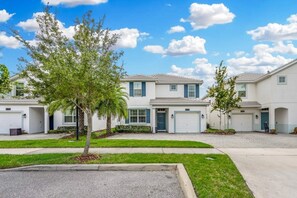 A row of two-story townhouses with attached garages, a well-maintained lawn, and a clear blue sky. - 5BR Villa Private Pool & Lake View (Kissimmee)