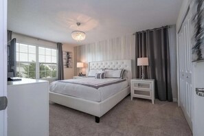 Une chambre à coucher avec un grand lit, des tables de chevet, un lustre, des rideaux et une fenêtre avec des stores.