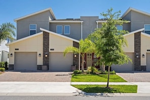 A modern residential building with a symmetrical facade, numbered units, and a well-maintained front yard with trees and shrubs. - Cozy 3BR in Champions Gate With Amazing Views! (Davenport)