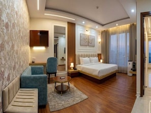A hotel room with a bed, a seating area with a chair, a small table, and a television mounted on the wall. - Deluxe 66 Inn Guest House (Bidhannagar)