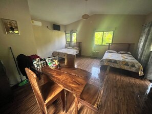 A room with a wooden dining table, two beds with patterned bedding, a window with curtains, and a wall-mounted TV. - Cozy 2-bedroom cabin in nature full Puerto Viejo, Limon, Costa Rica (Limón)