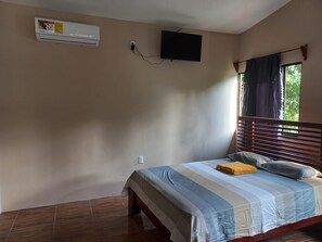 Ein Schlafzimmer mit einem Bett, einer Klimaanlage, einem Fernseher und einem Fenster mit Vorhängen.
